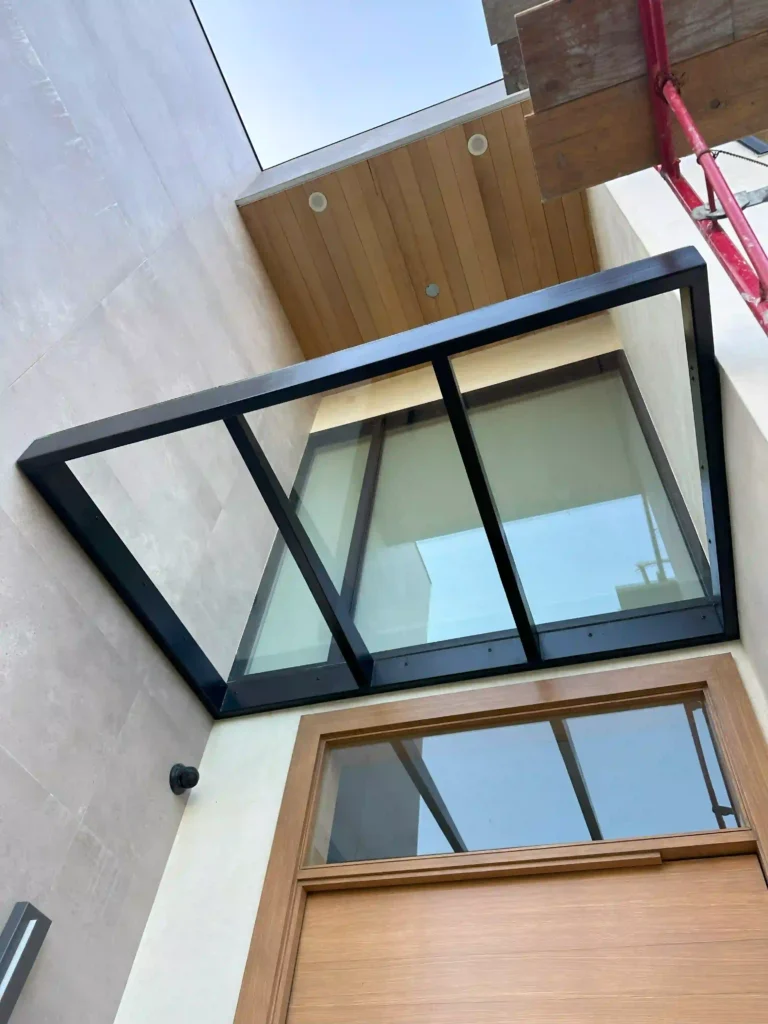 Modern glass awning with black metal frame installed above a wooden door by Metro GDS Inc.