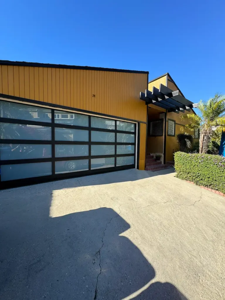 Exterior view of modern frosted glass garage door installation on a yellow home in Encino, CA by Metro GDS