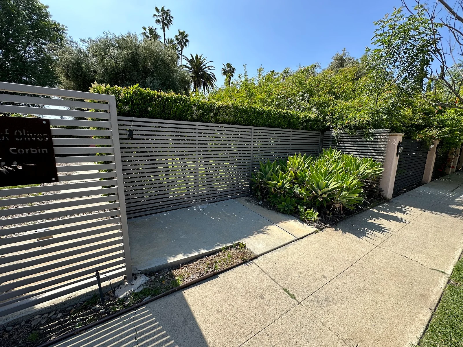 Modern horizontal slat driveway gate and matching privacy fence in a taupe finish with an engraved address plaque